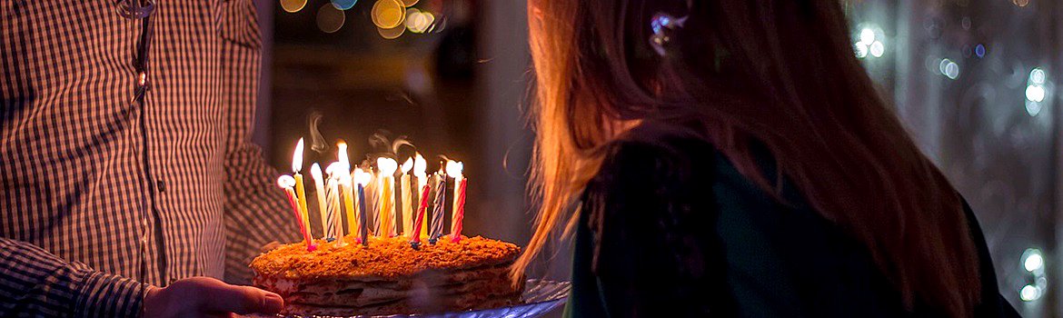 Zdjęcie osoby wręczającej tort urodzinowy ze świeczkami. Zdjęcie jest banerem strony - cukiernia online wypieki z dostawą